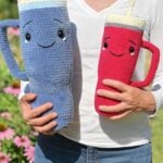 A person holding two crochet Amigurumi tumblers, one jumbo gray and one hot pink, both with smiling faces.