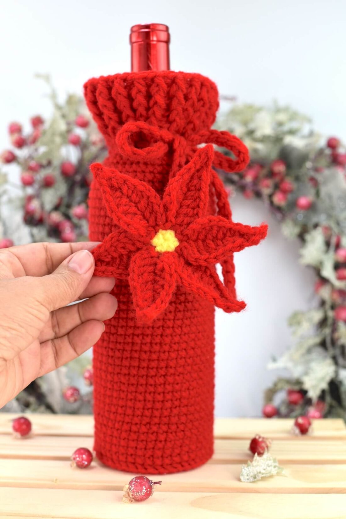 Crochet wine bottle cozy with ribbed neck and red poinsettia flower drawstring detail.