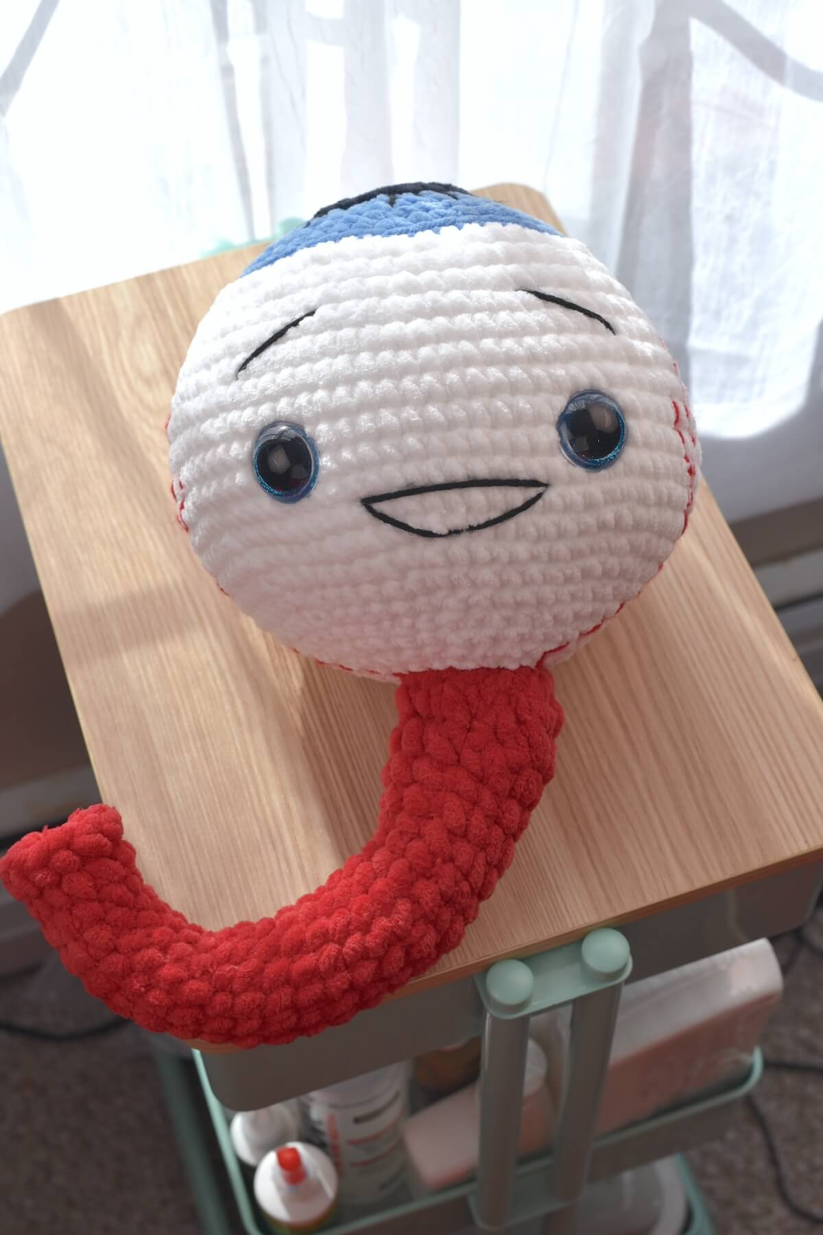 Oversized Amigurumi crochet eyeball plushie with blue iris, made with soft chenille yarn, perfect for spooky Halloween craft.