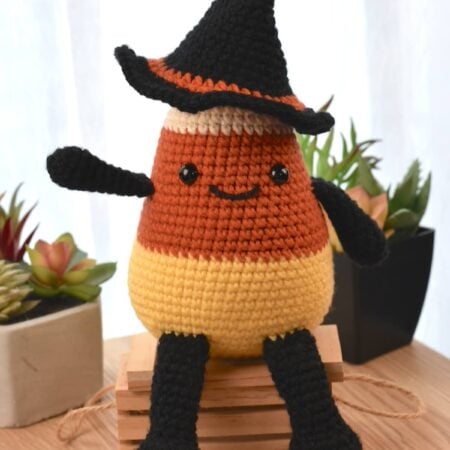 Cute crochet Halloween plushie shaped like a candy corn, with black crocheted arms, legs, and a smiling embroidered face.
