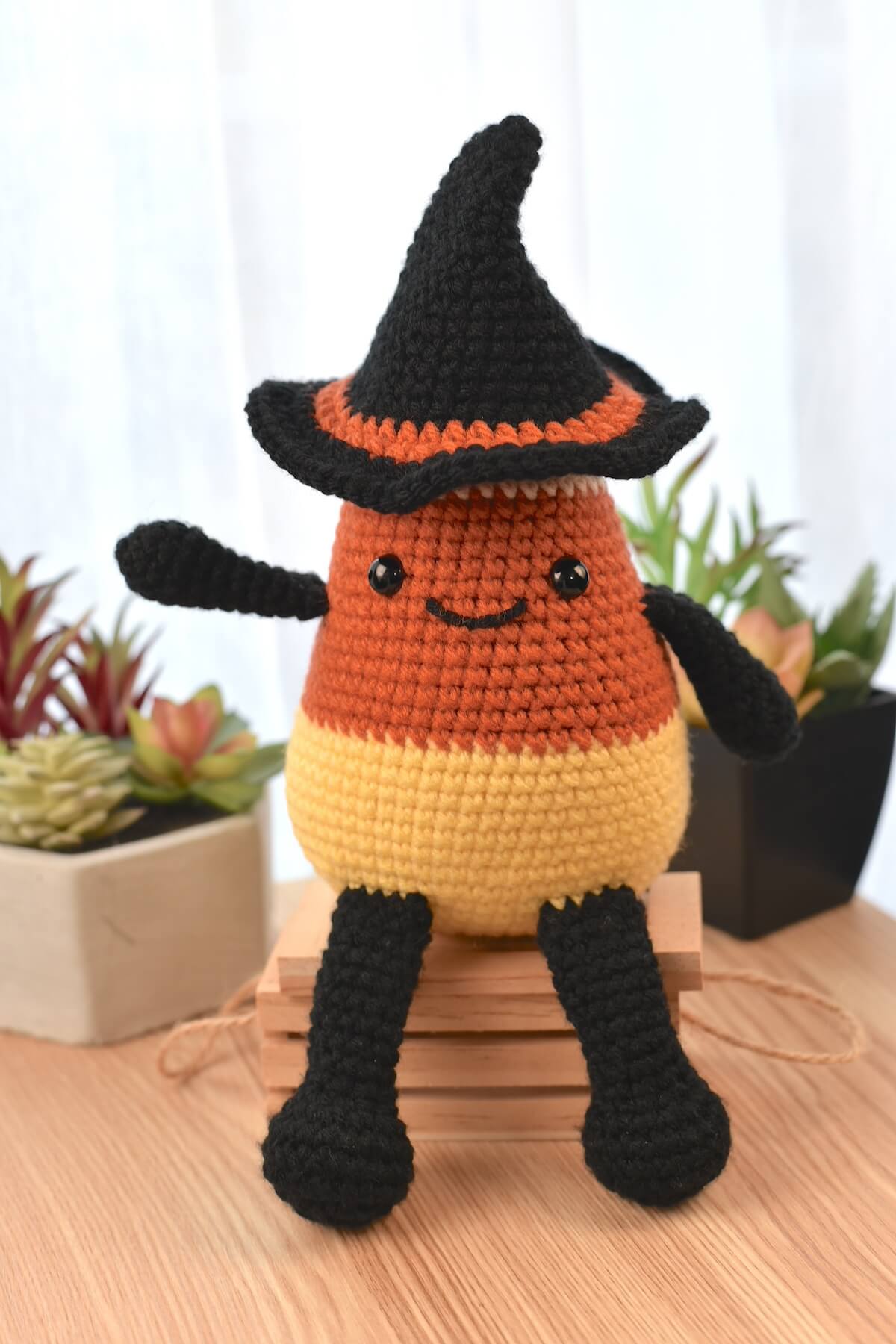 Halloween crochet candy corn plushie with black limbs and pointed witch hat, displayed as a festive decoration.