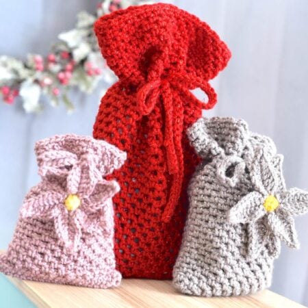 Red crochet drawstring mesh gift bag standing beside two smaller crochet pouches in neutral tones.