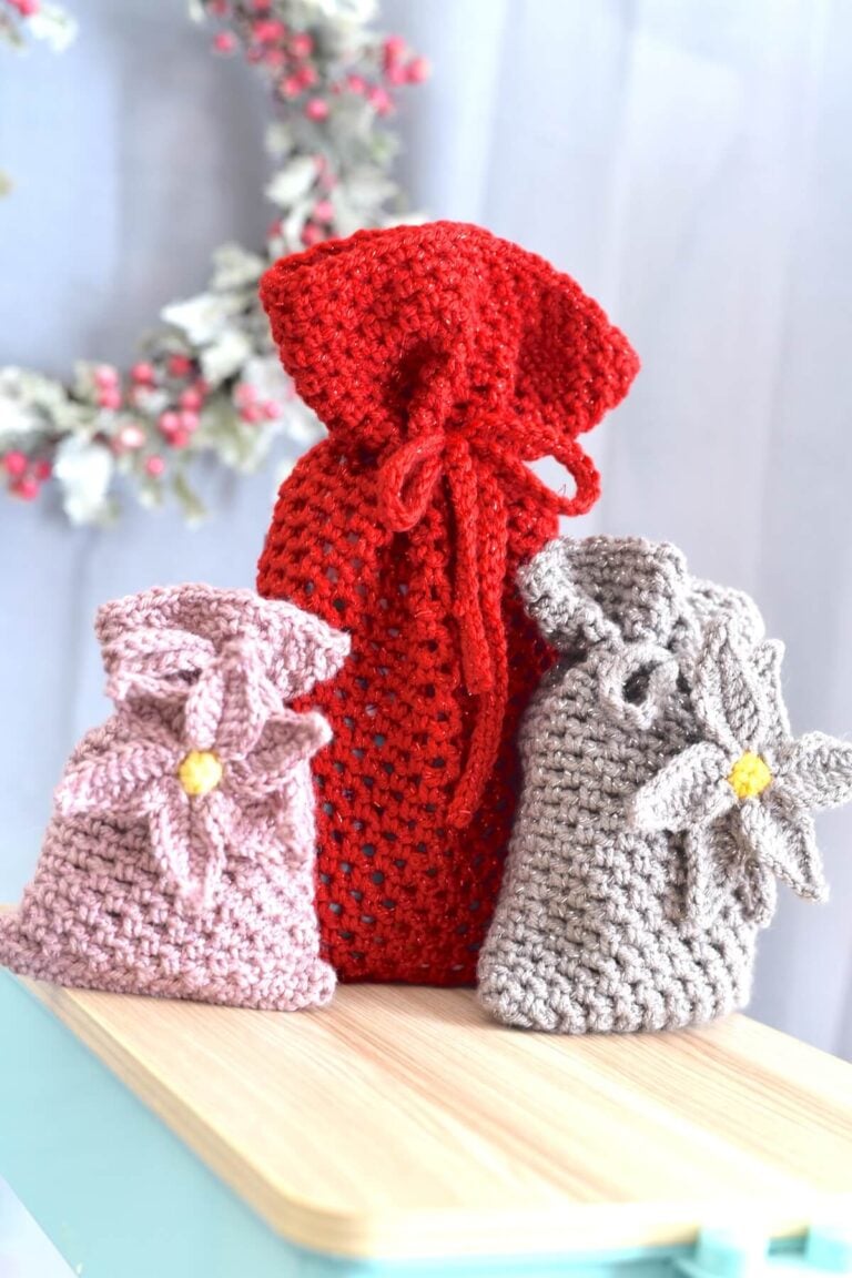Red crochet drawstring mesh gift bag standing beside two smaller crochet pouches in neutral tones.