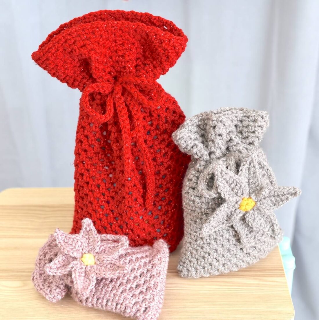 Crochet gift bag pattern in three sizes with one red mesh bag and two textured smaller bags.