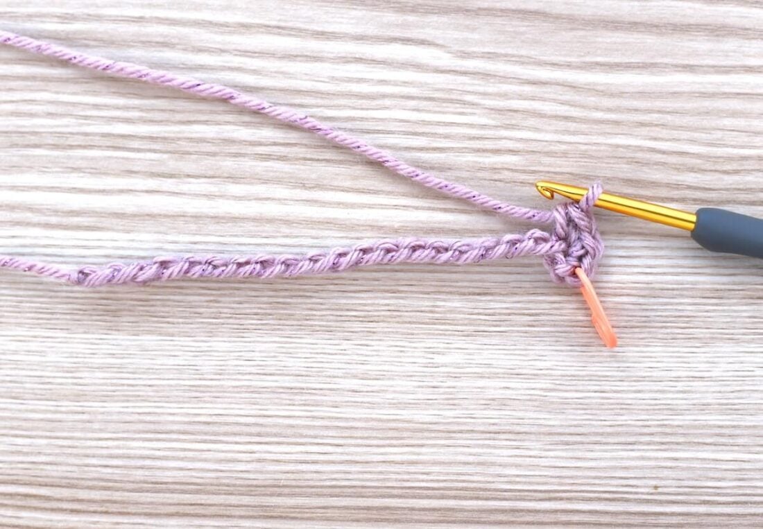 Starting round of the crochet gift bag pattern base using pink sparkly yarn and a gold crochet hook.