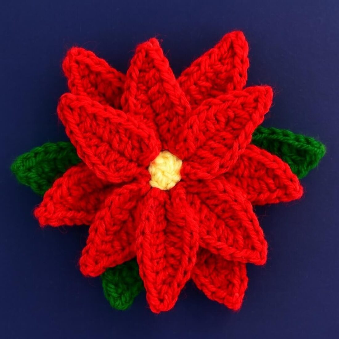 Layered crochet poinsettia flower with classic red and green and a yellow center displayed flat.
