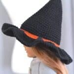 Side view of a black crochet witch hat with an orange band displayed on a American Girl doll's head.