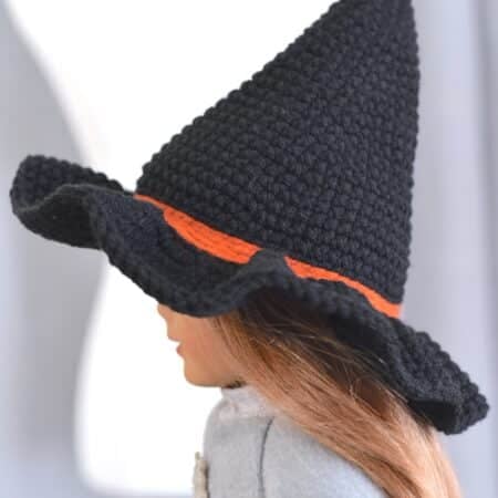 Side view of a black crochet witch hat with an orange band displayed on a American Girl doll's head.