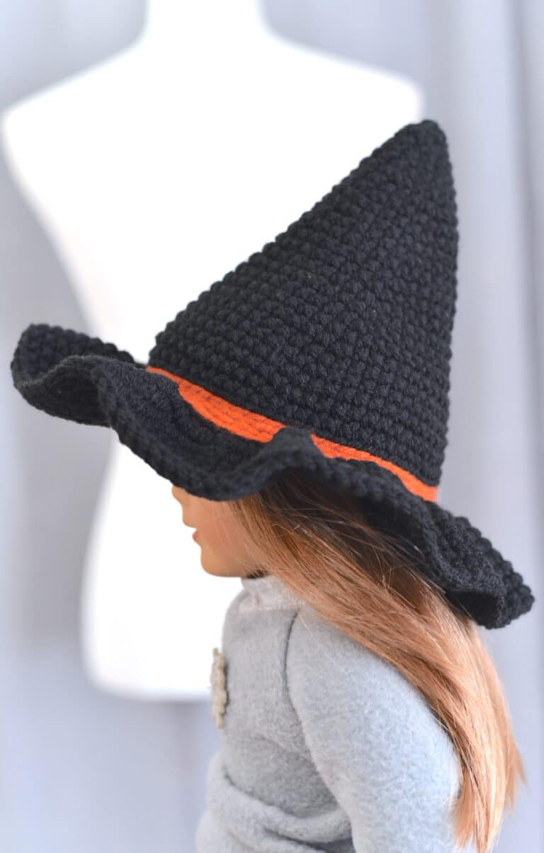 Side view of a black crochet witch hat with an orange band displayed on a American Girl doll's head.
