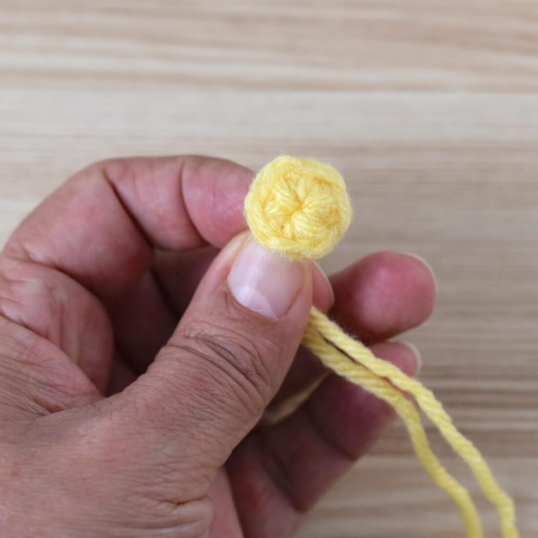 A hand holding a small crochet circle made with yello yarn.