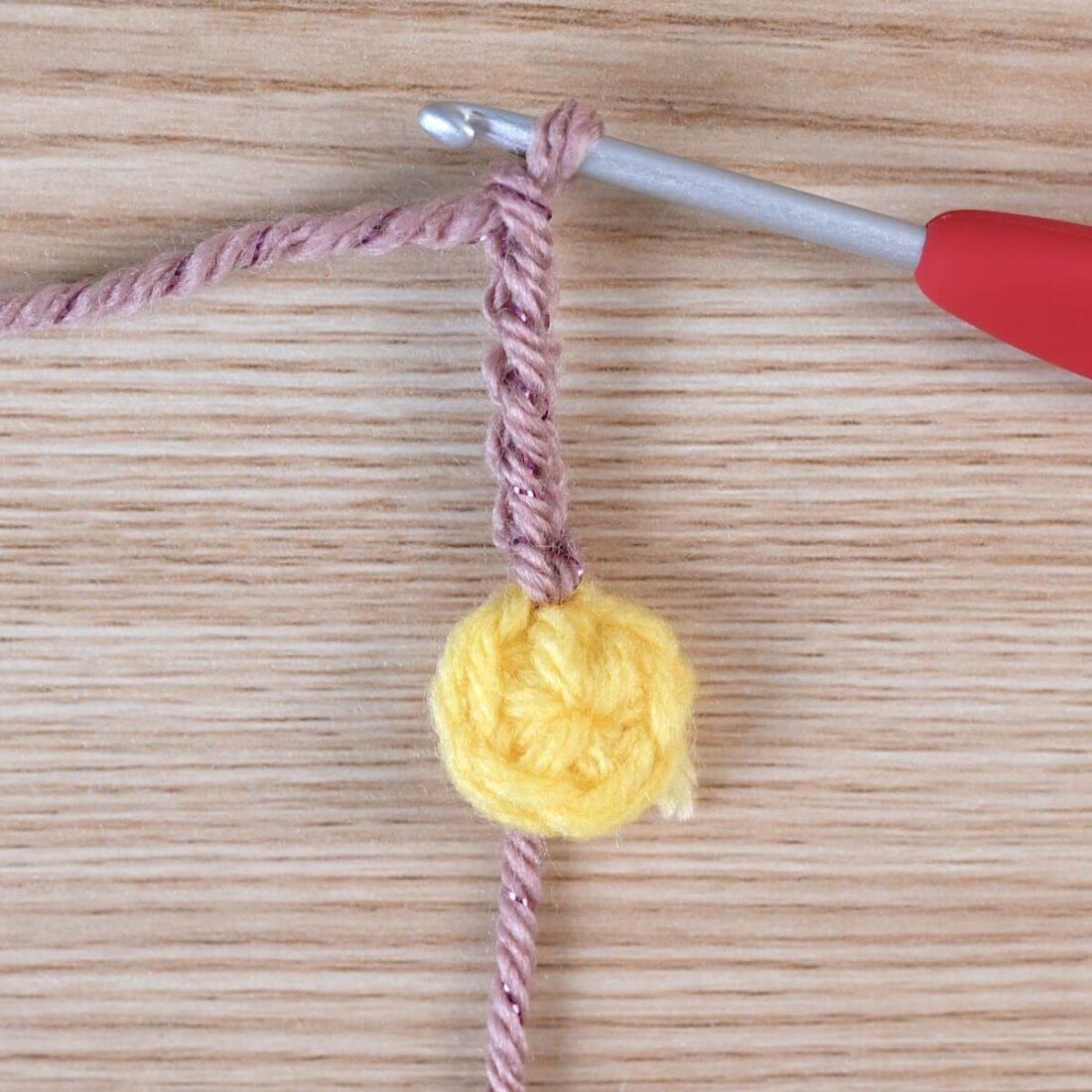 Yellow crochet circle and the start of a poinsettia flower petal with a silver crochet hook.