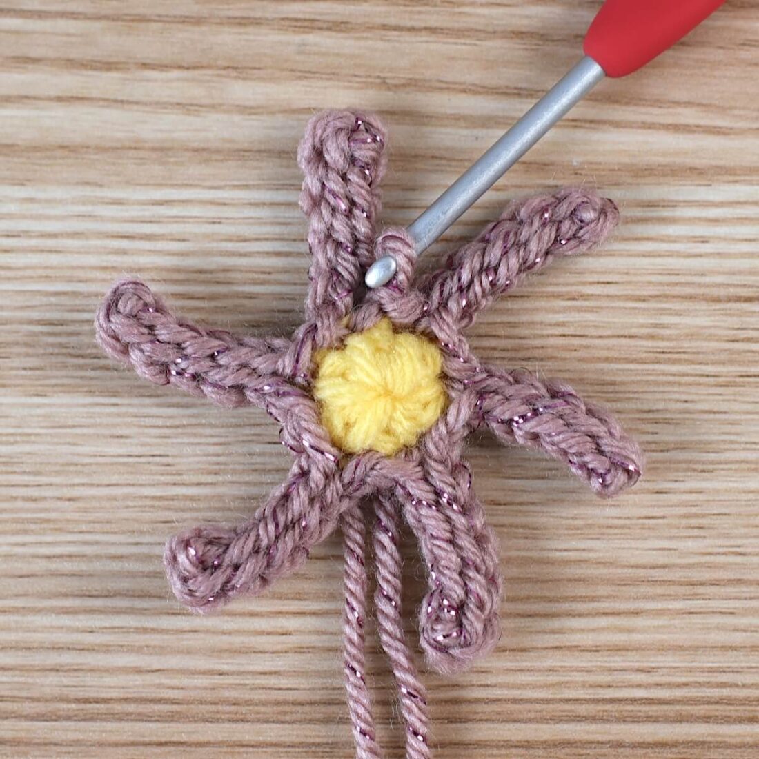 Yellow crochet circle and pink yarn showing the early stage of a poinsettia flower with a silver crochet hook.