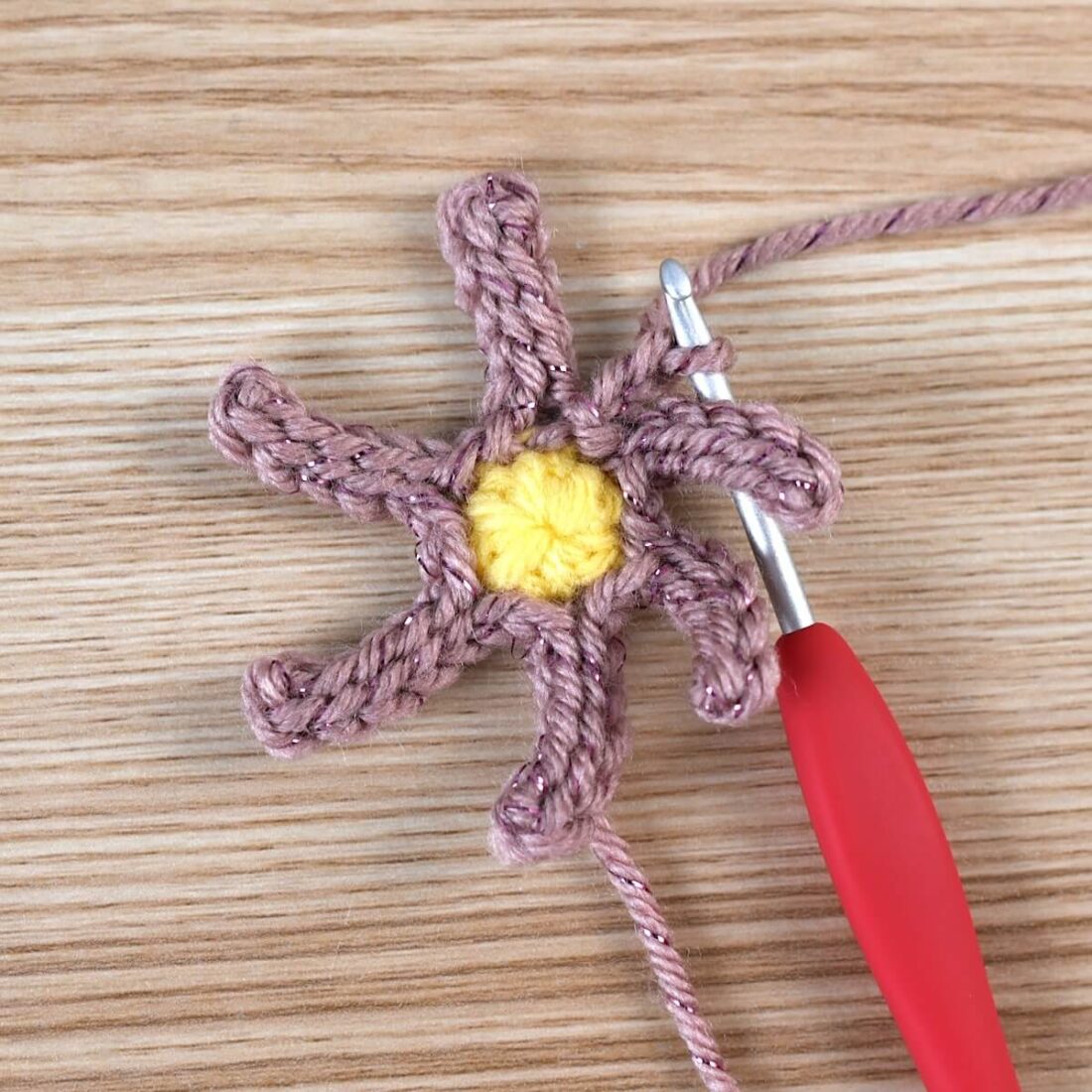 ellow crochet circle and pink yarn showing the early stage of a poinsettia flower with a silver crochet hook.
