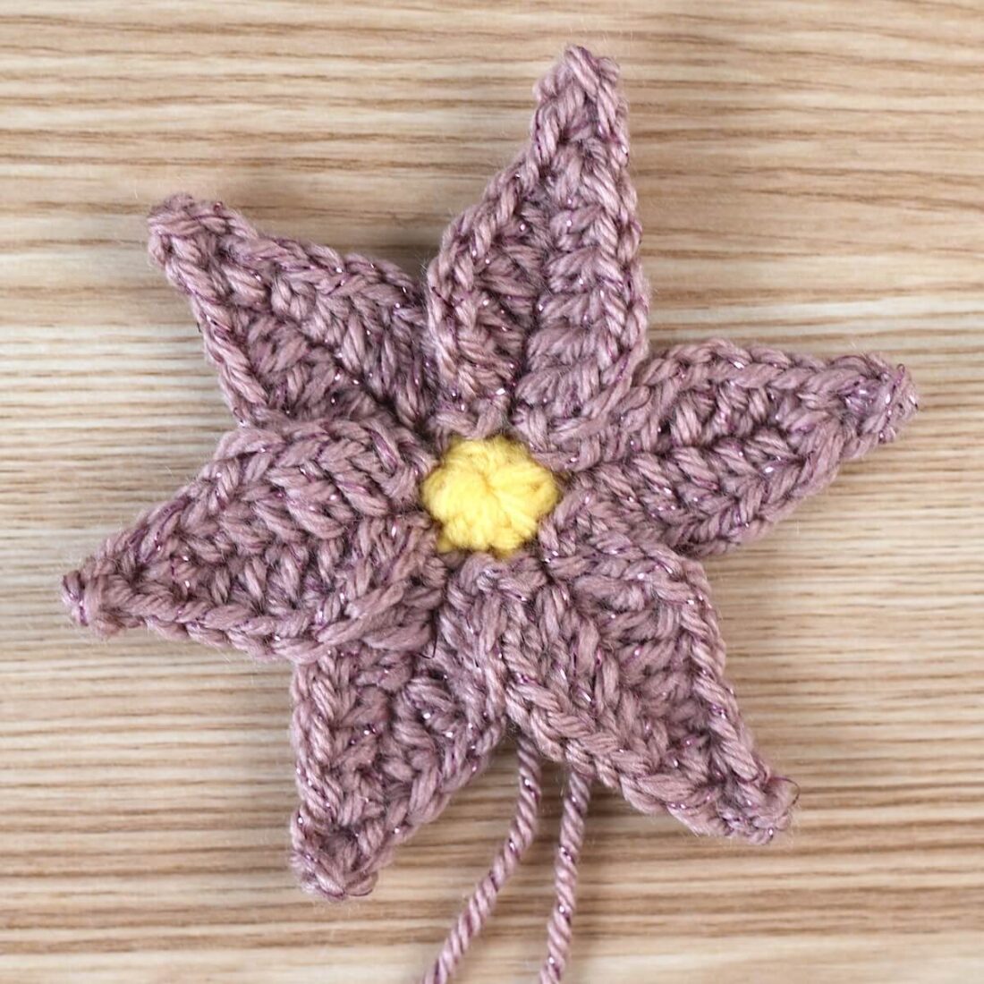 A crochet poinsettia flower made with yellow and pink yarn.
