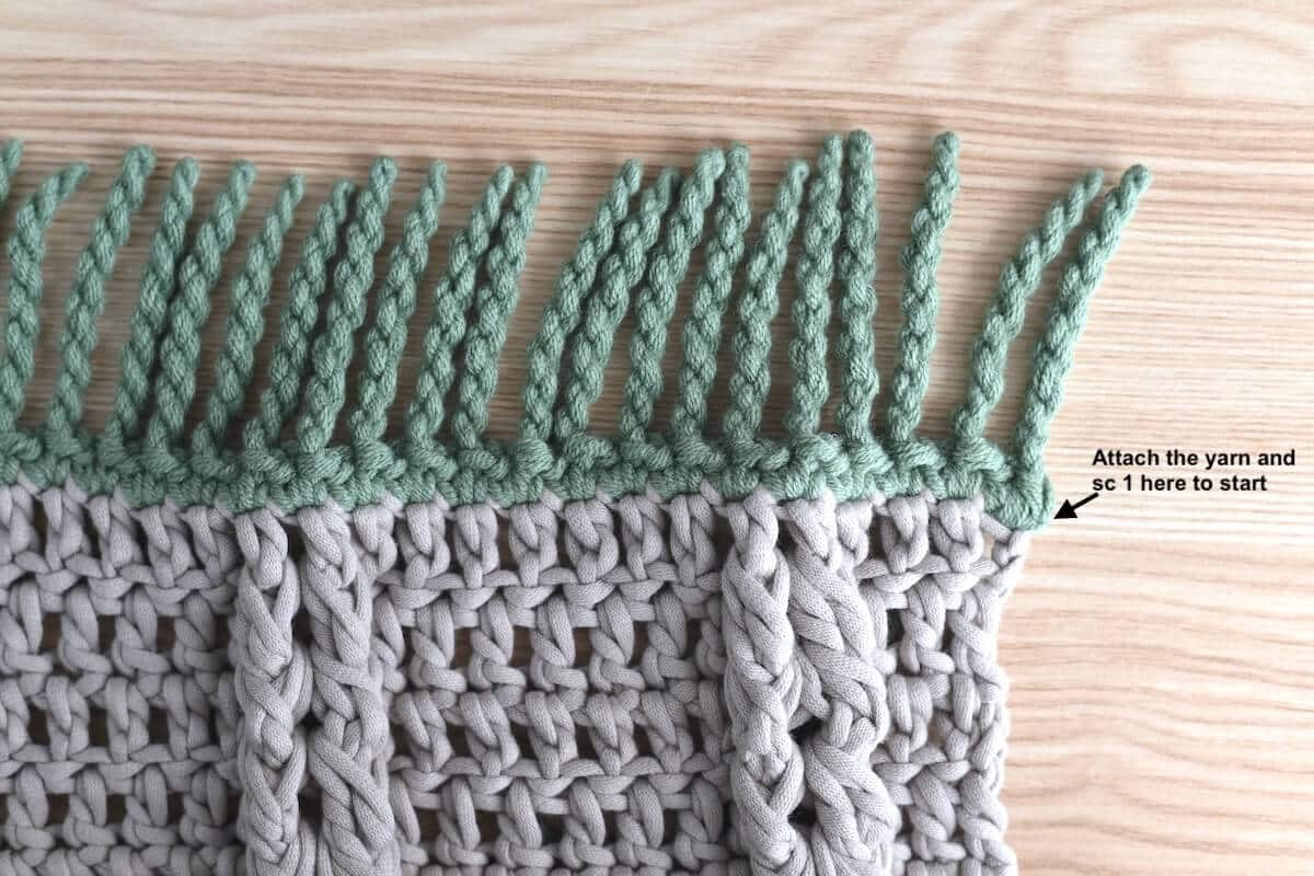 A close-up of a brown crochet swatch with a green twisted fringe.