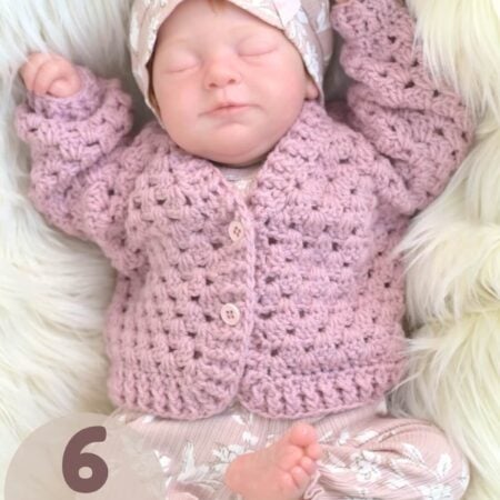 A life-like, asleep reborn baby doll dressed in a pink crochet baby cardigan.