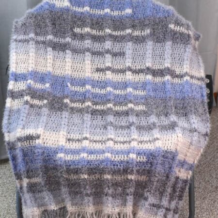 Crochet blanket draped over a chair, featuring ribbed texture and color blocks of gray, blue, and white.