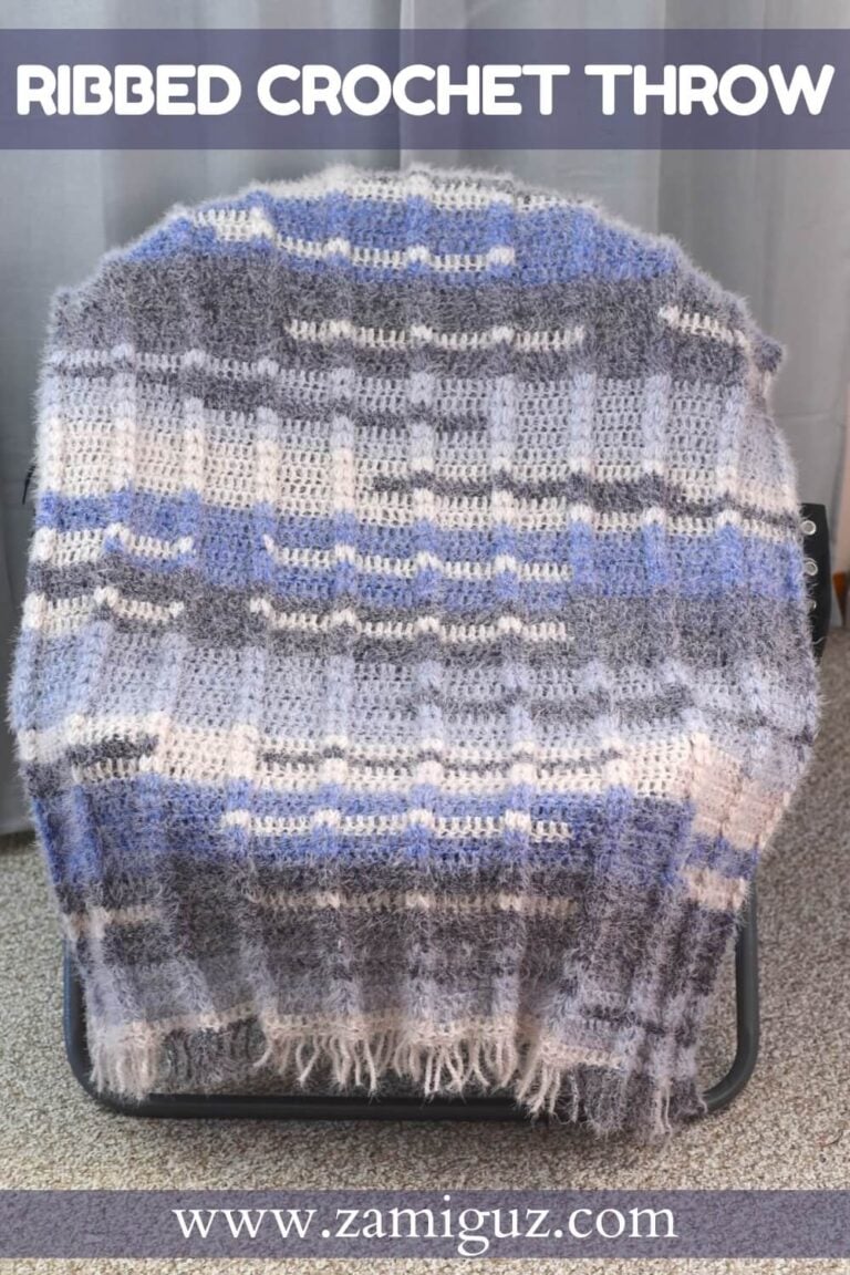 Crochet blanket draped over a chair, featuring ribbed texture and color blocks of gray, blue, and white.