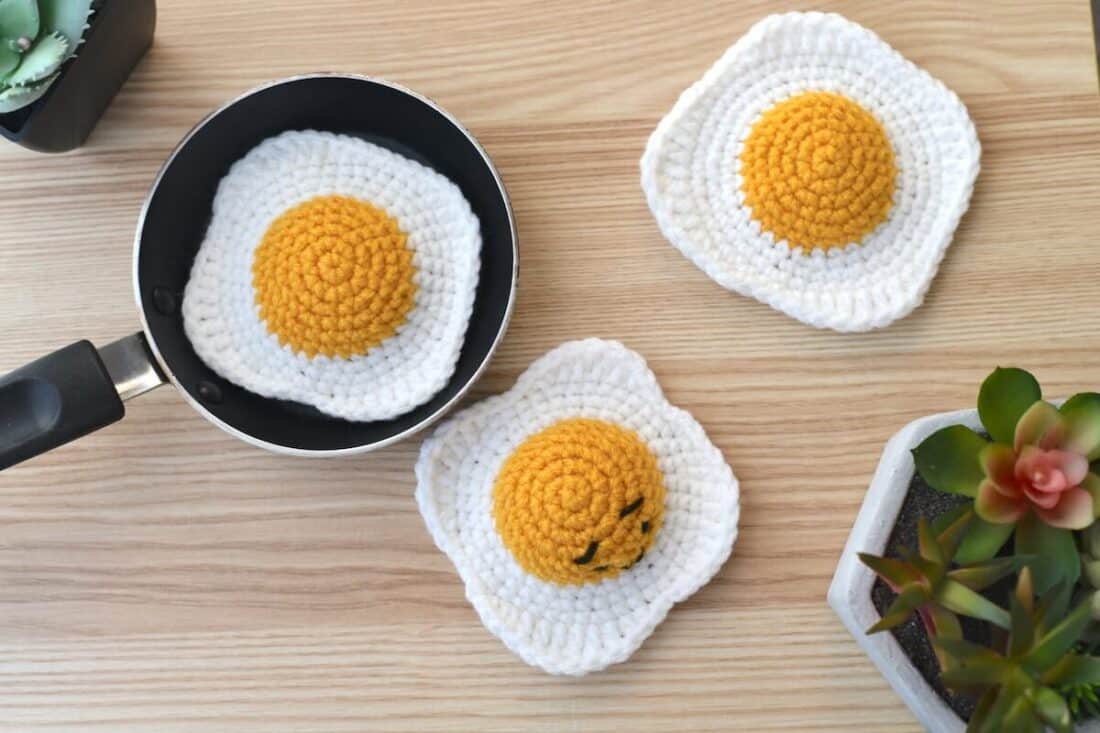 A close-up view of three crochet fried eggs showcasing the dimensional stitches used to create a puffy yolk and gently rippled egg white.