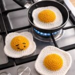 Three realistic crochet fried eggs on top of a kictchen stove.