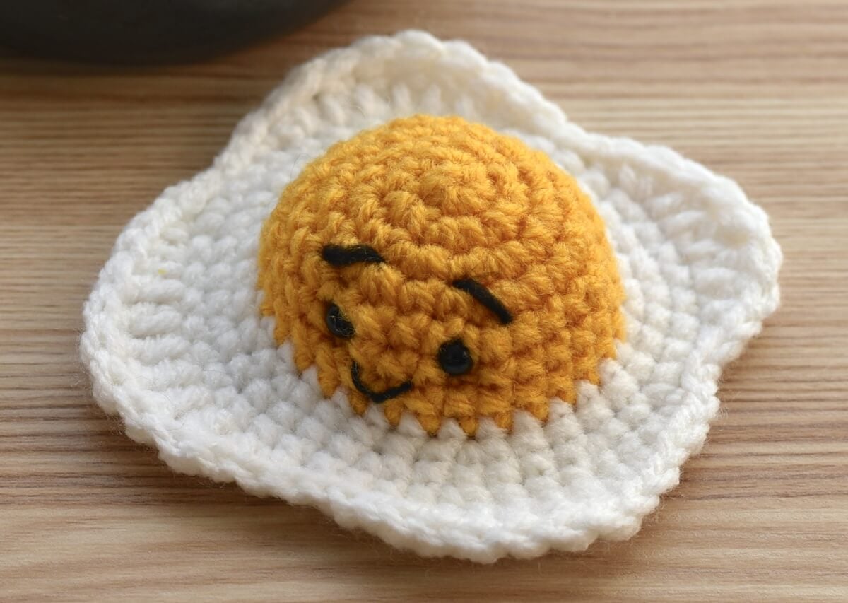 Embroidering a cute face onto the crochet fried egg.