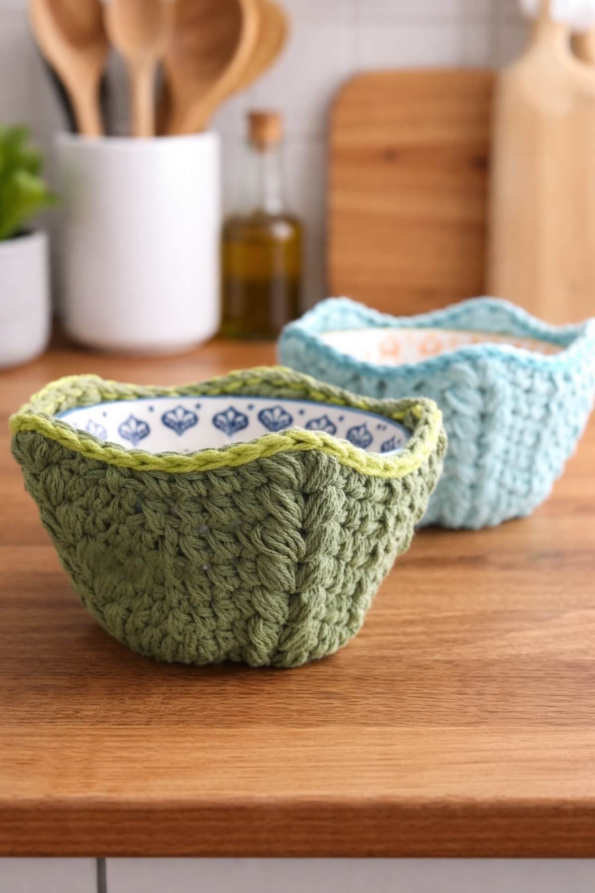 A close-up view of two crocheted soup bowl holders featuring beautiful textured stitches, designed for heat protection and photographed on a wooden countertop.