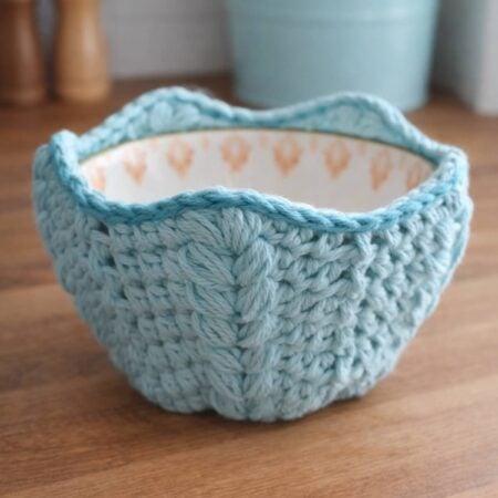 Handmade crochet bowl holder in light blue cotton yarn on a wooden kitchen counter