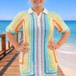 Woman standing on an wooden deck on a sunny beach, wearing a colorful, striped hexagon crochet dress.