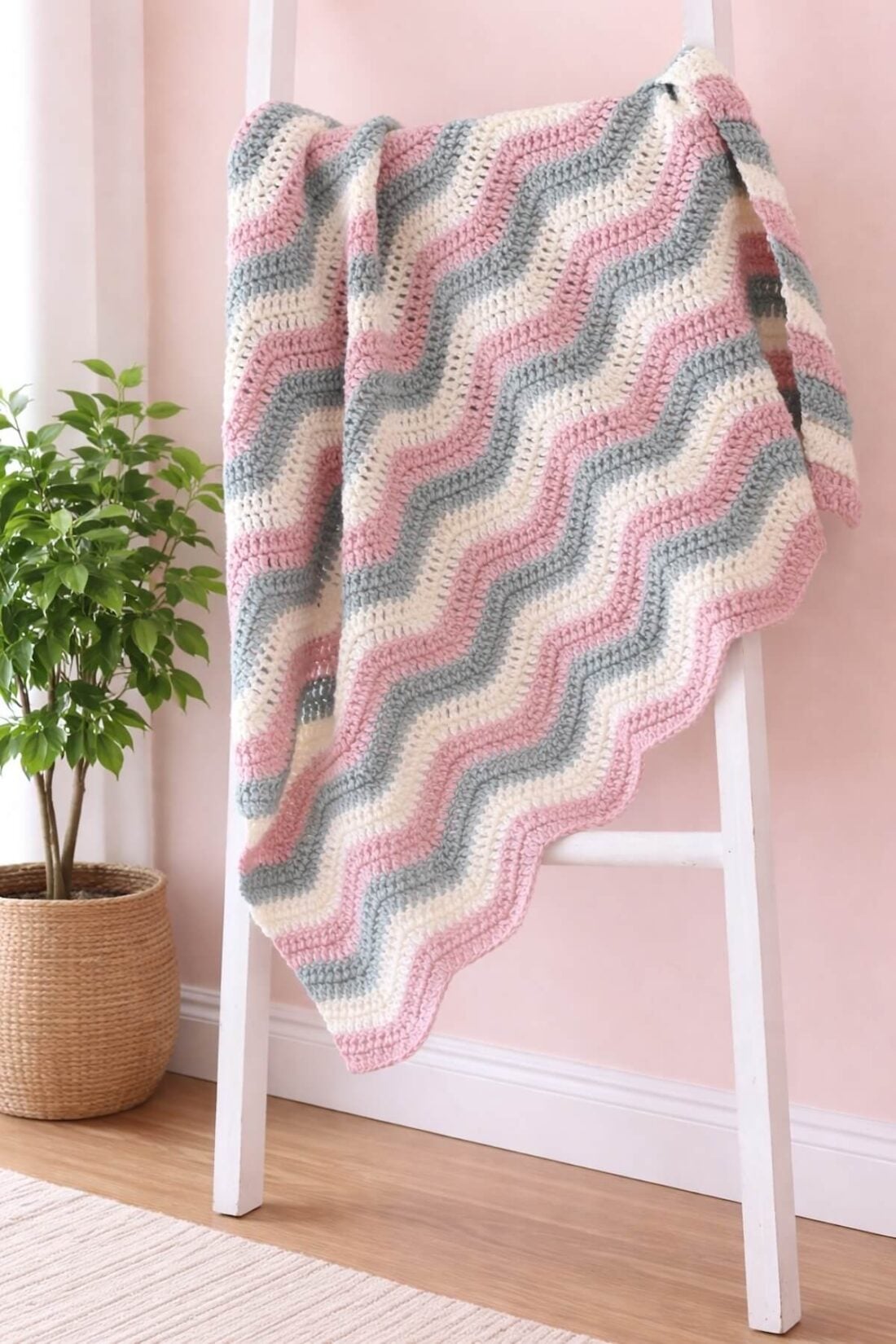 Ripple stitch crochet afghan with soft pink, green, and cream yarn draped over a white ladder.