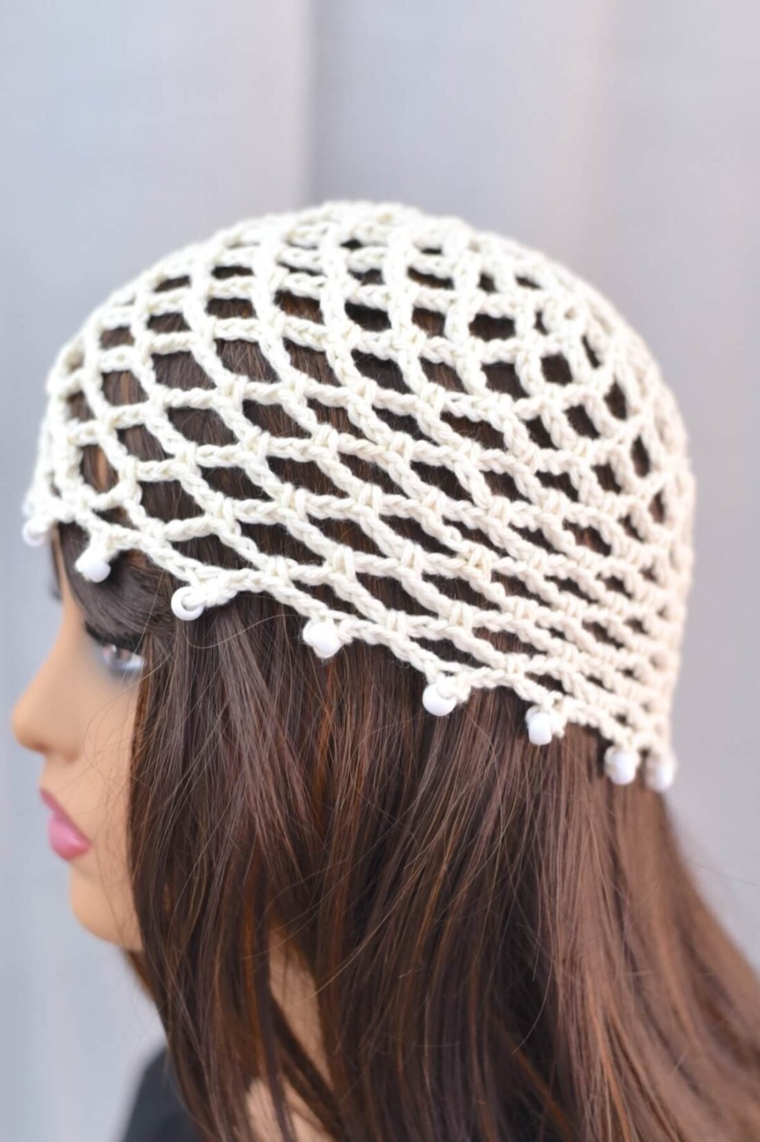 Side profile of an off-white crochet mesh hat with edges decorated with beads