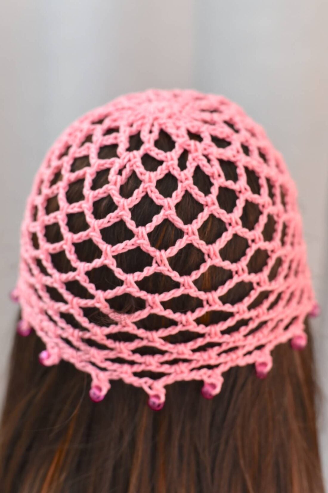 Back view of a crochet skull cap made with a mesh stitch on a brunette mannequin
