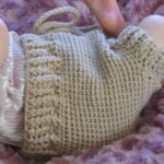 A close-up of a beige crochet baby bloomers modeled on a reborn doll