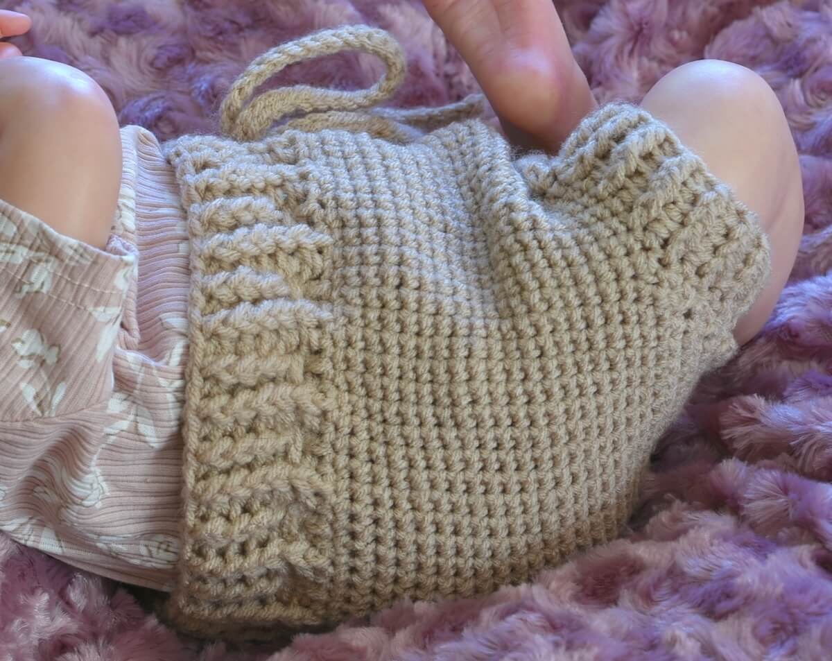 A close-up of a beige crochet baby bloomers modeled on a reborn doll
