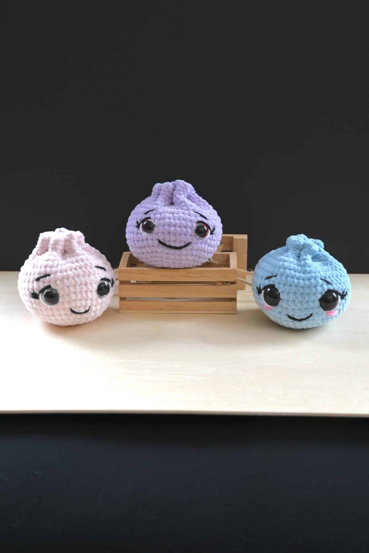 Blue, pink, and purple crochet dumplings with sweet embroidered facial details.