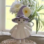 Crochet witch doll wearing a purple pointed hat and white skirt, standing on the bottom of a basket.